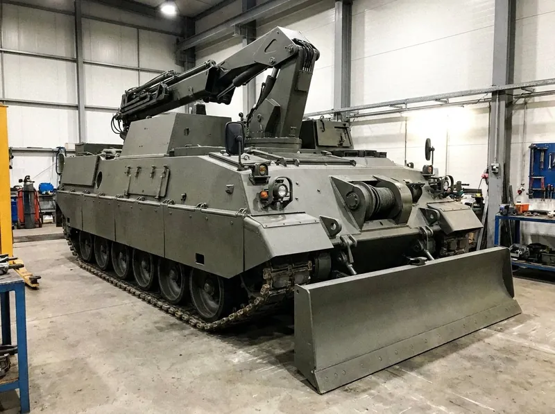 Illustrative image, not a delivered installation — a plain heavy tracked armoured recovery vehicle with no turret and no gun, its hydraulic crane boom raised, a front dozer / earth-anchor spade blade and a heavy winch fairlead, on a workshop hardstanding, matte and unmarked, no text and no people