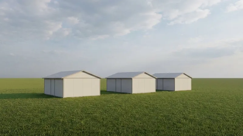A small cluster of three flat-pack modular disaster relief shelters with plain pitched roofs and light-coloured wall panels, standing directly on open grass with no visible foundation, and no people