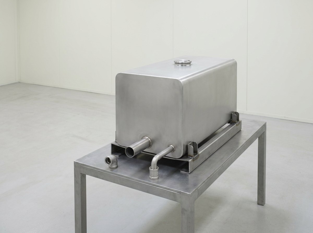 A single plain metal fuel tank on a steel cradle, with a feed pipe and a vent pipe leaving its underside and a round inspection port on top, and no people