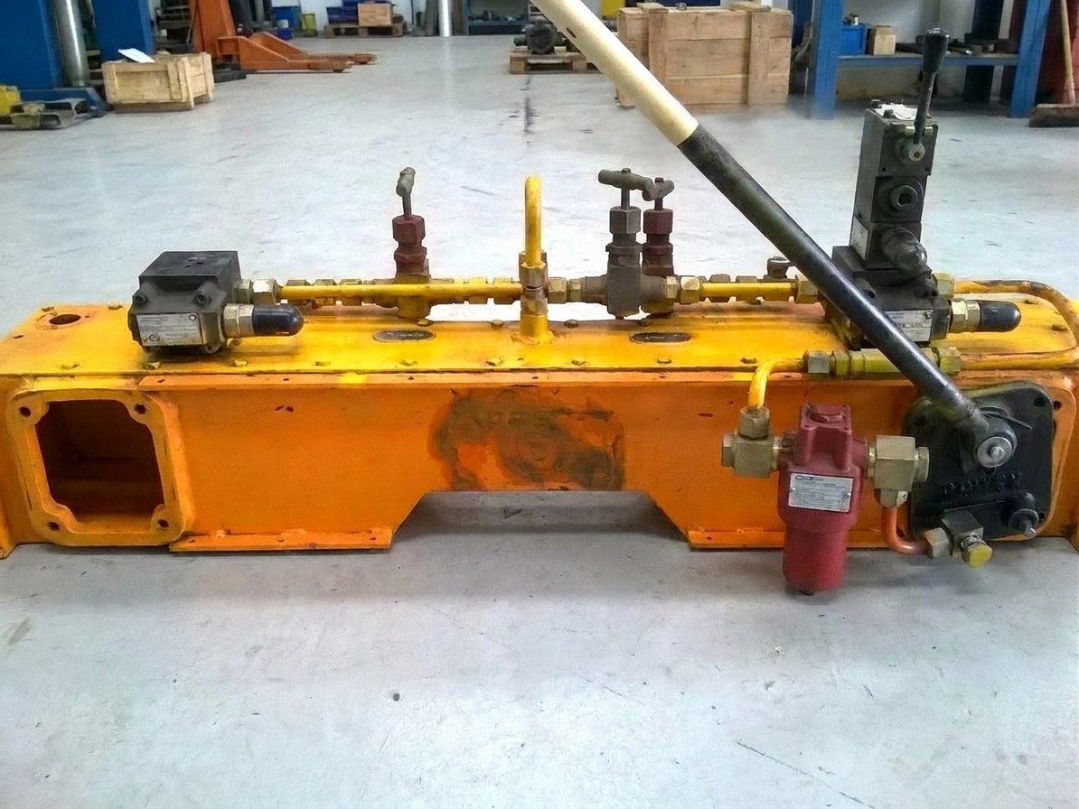 As-received Russian-origin hydraulic power beam of a Su-30 MKI installation trolley at the Neometrix works — worn orange fabricated beam with hand pump, direction control valve, needle valves and inline filter
